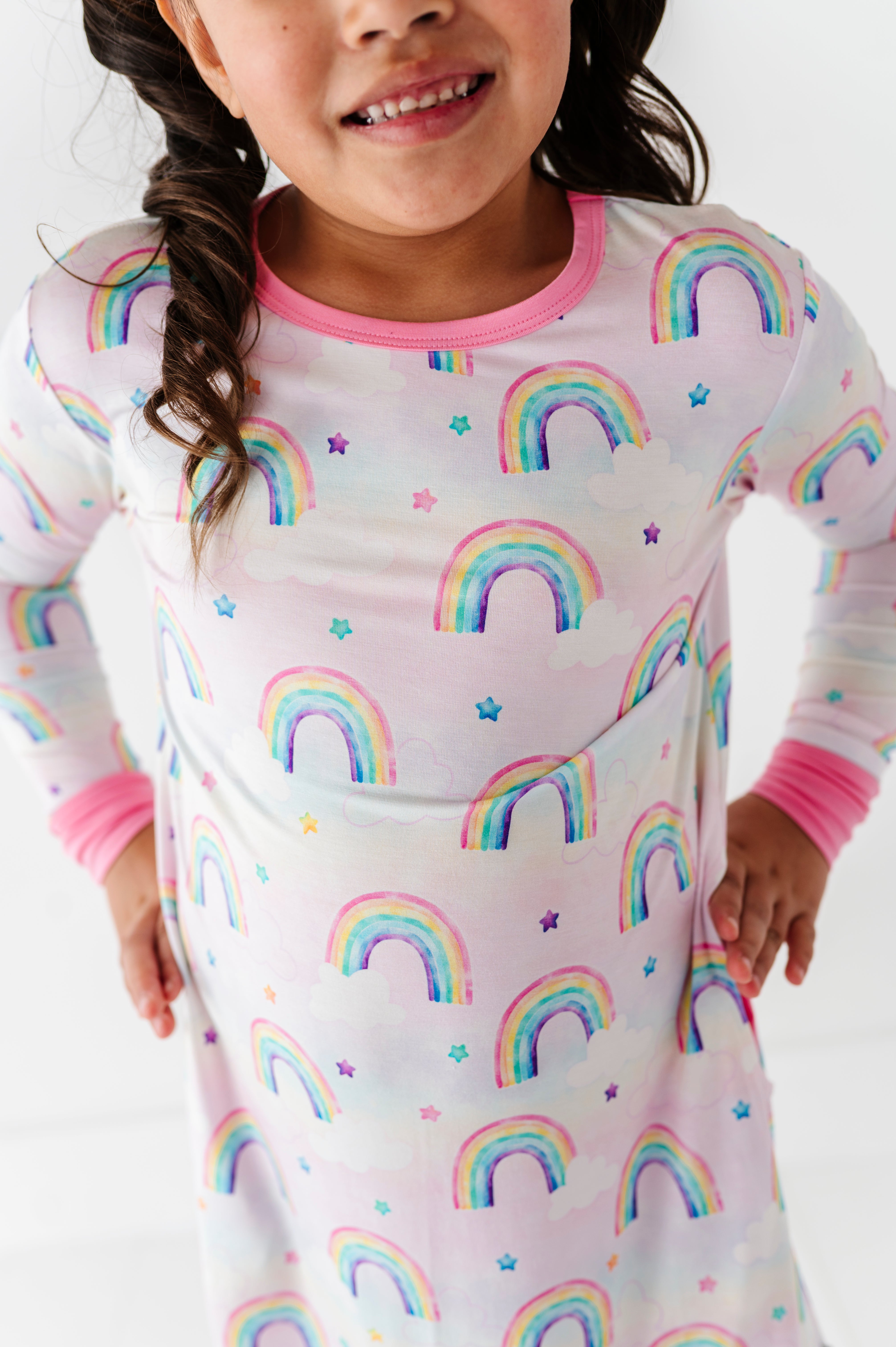 Child wearing a pink rainbow-patterned gown with a white background